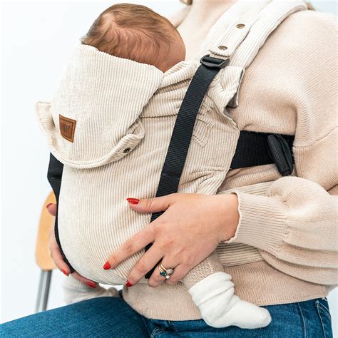 Illustratie van de TOMY Classic Beige draagzak met een baby die naar de drager toe kijkt.