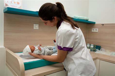 Een kraamverzorgende die een baby vasthoudt en een moeder begeleidt.