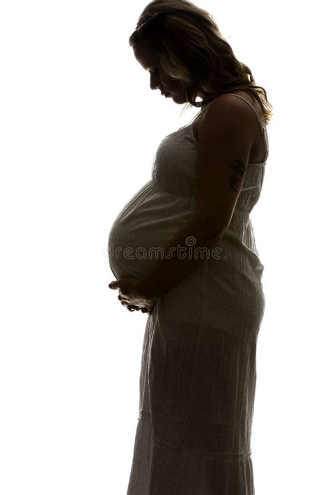 Zwart-wit silhouetfoto van een zwangere vrouw bij een raam