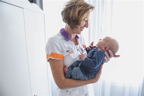 Foto van een lachende kraamverzorgende die een baby vasthoudt