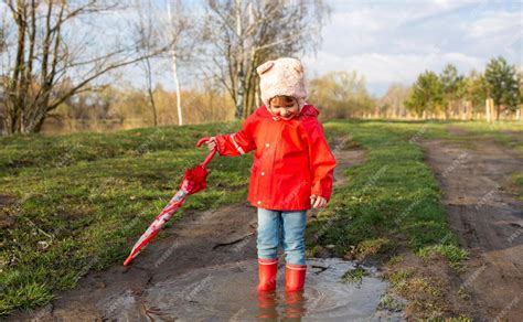 kind met regenjas en laarzen die vrolijk buiten speelt
