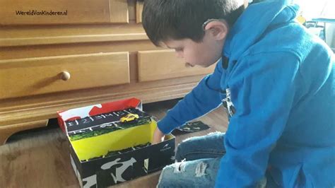 Een kind bouwt een speelwereld voor zijn dieren met behulp van een schoenendoos, blauw papier en tekeningen.