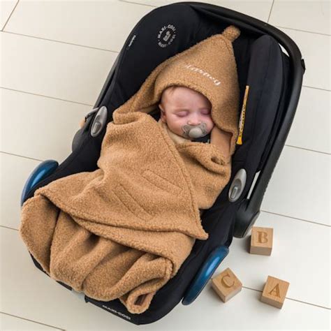 Baby in een autostoel, warm gewikkeld in een deken met openingen voor de gordels