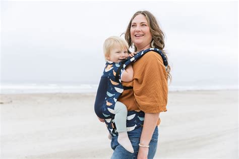 Een baby speelt veilig in een draagzak op het strand, met de zee op de achtergrond.