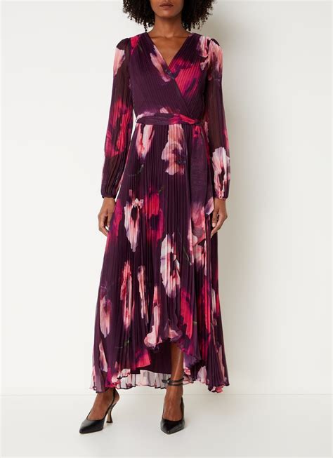 Een vrouw in een elegante maxi-jurk met bloemenprint, met haar handen op haar zwangere buik.