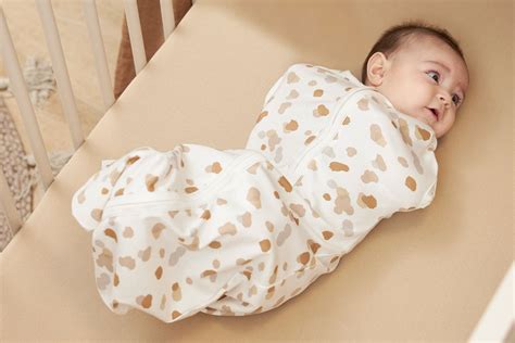 Illustratie van een baby die zachtjes rolt in bed, met een inbakerslaapzak ernaast.