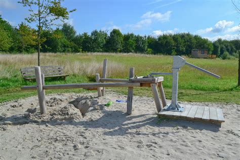 Ruime buitenspeelplaats met speeltoestellen, zandbak en waterpomp.