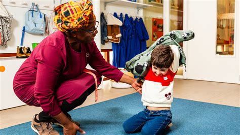 Ouder die een peuter helpt met het aantrekken van een jas, met nadruk op het zelf doen van de rits.
