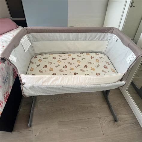 Illustratie van een co-sleeper die aan een volwassen bed is bevestigd, met een baby erin.
