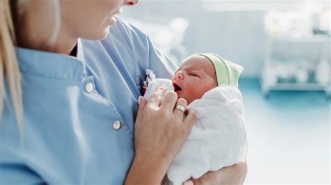 Foto van een kraamverzorgende die een baby vasthoudt en lachend naar de ouders kijkt.