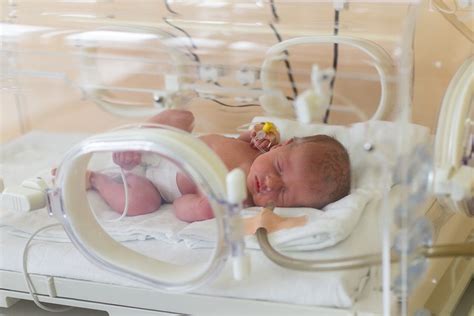 Foto van een baby in een couveuse met medische apparatuur.